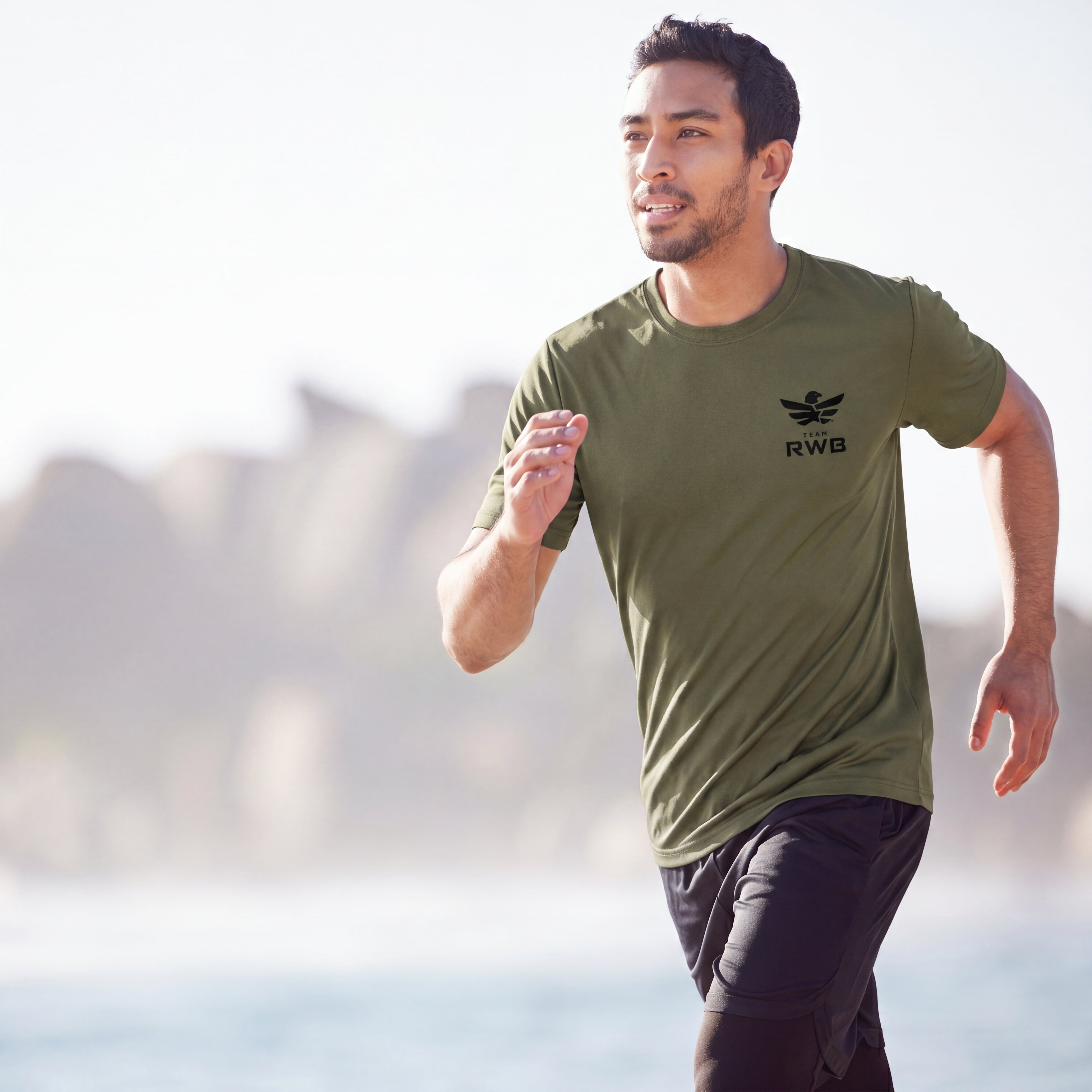 Man running outdoors wearing a green t-shirt with a logo.