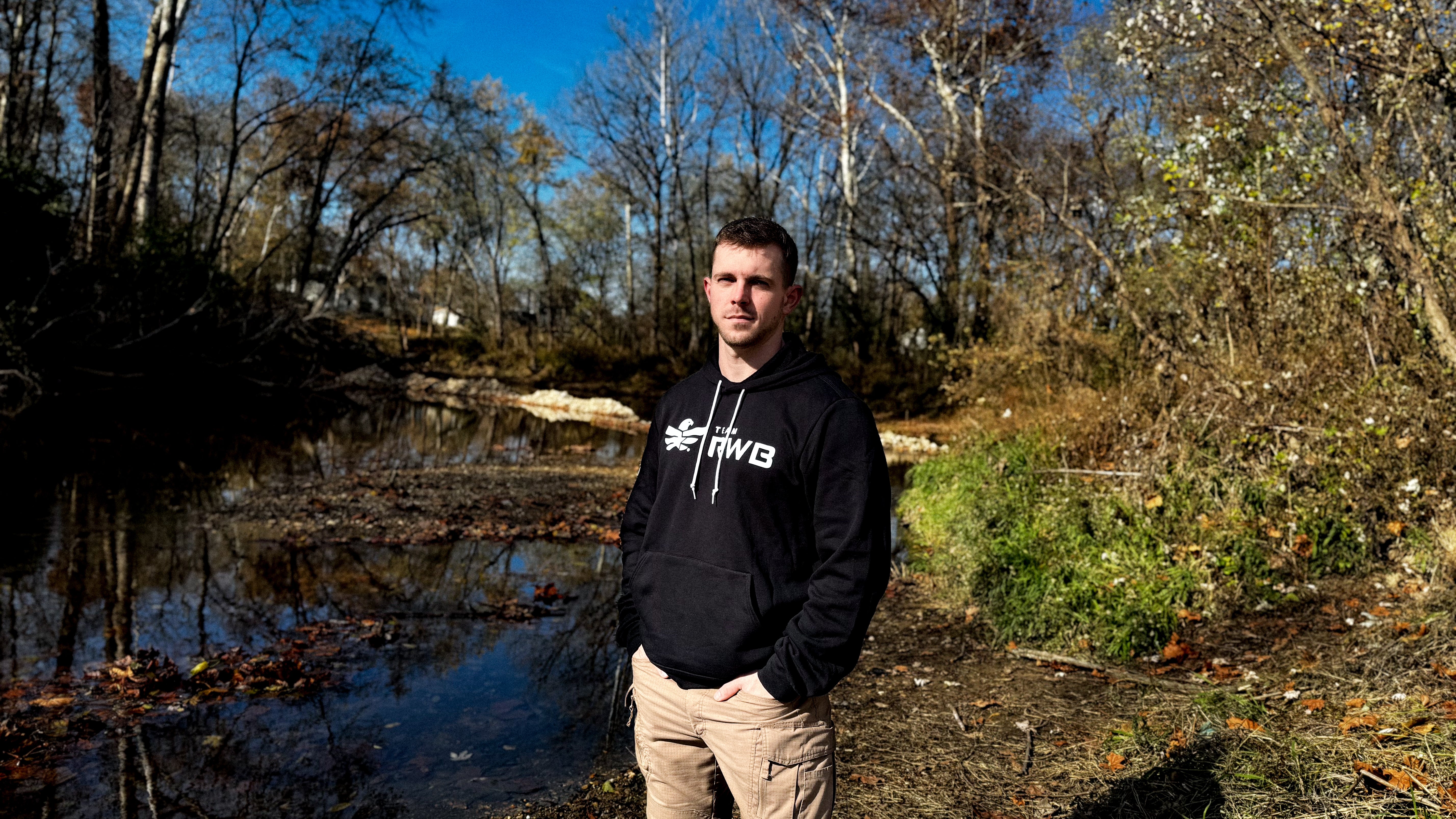 Man wearing black Team RWB hoodie outdoors in a wooded setting, front view showing Eagle graphic