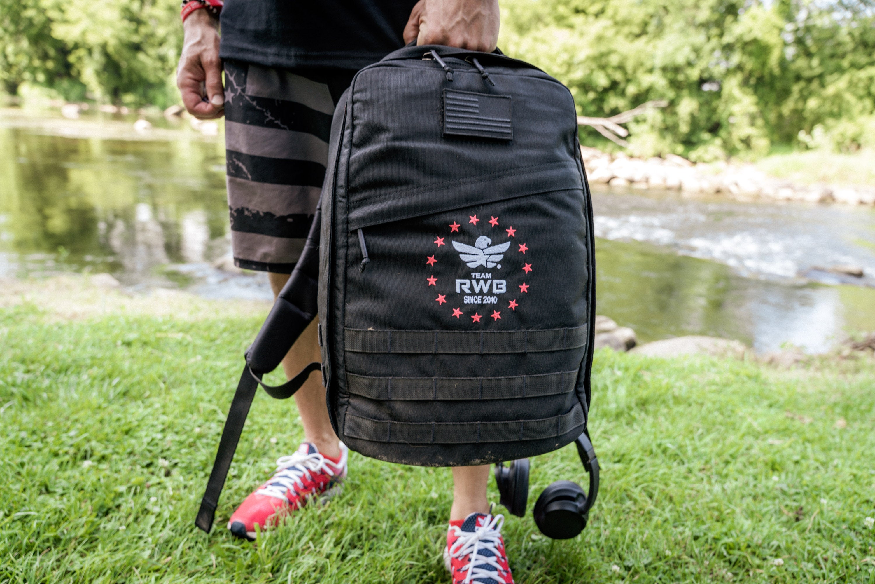 Team RWB Legacy GORUCK GR1 Rucksack worn outdoors – side profile showing MOLLE webbing and padded shoulder straps.