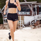Person running on a beach wearing black athletic wear with a visible brand logo.