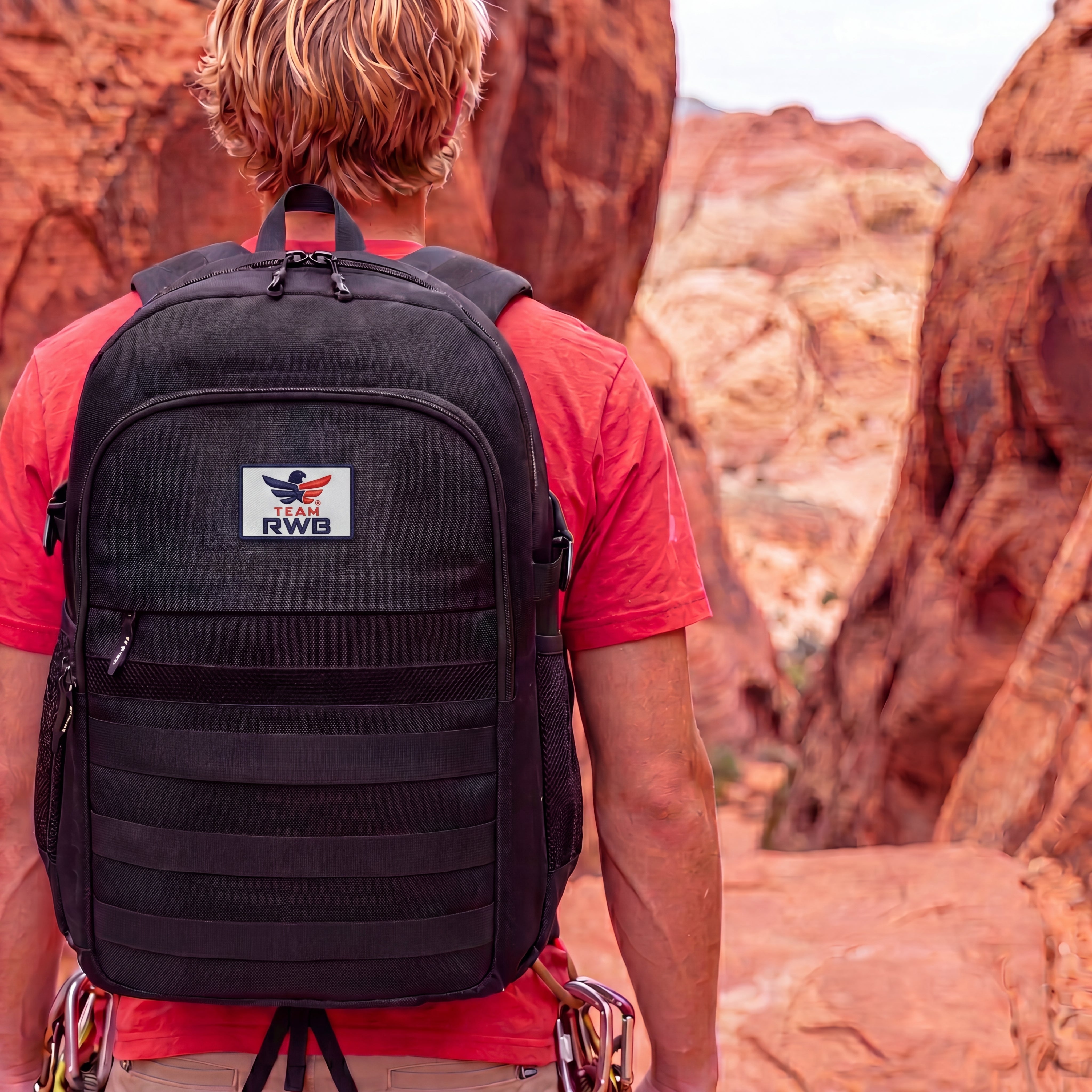 Person wearing a black backpack with a Team RWB logo in a desert landscape