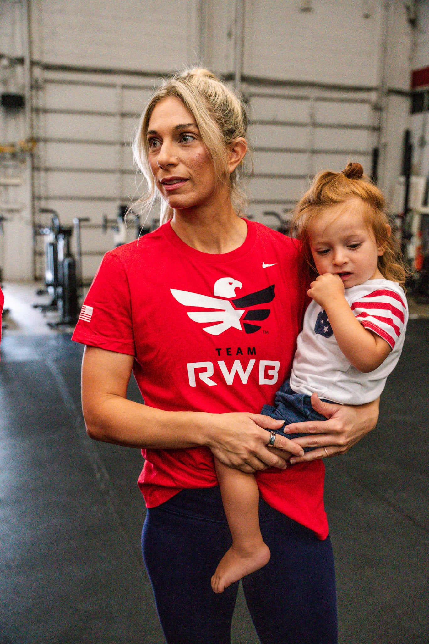 Team RWB member wearing Nike Dri-FIT T-Shirt holding child at gym