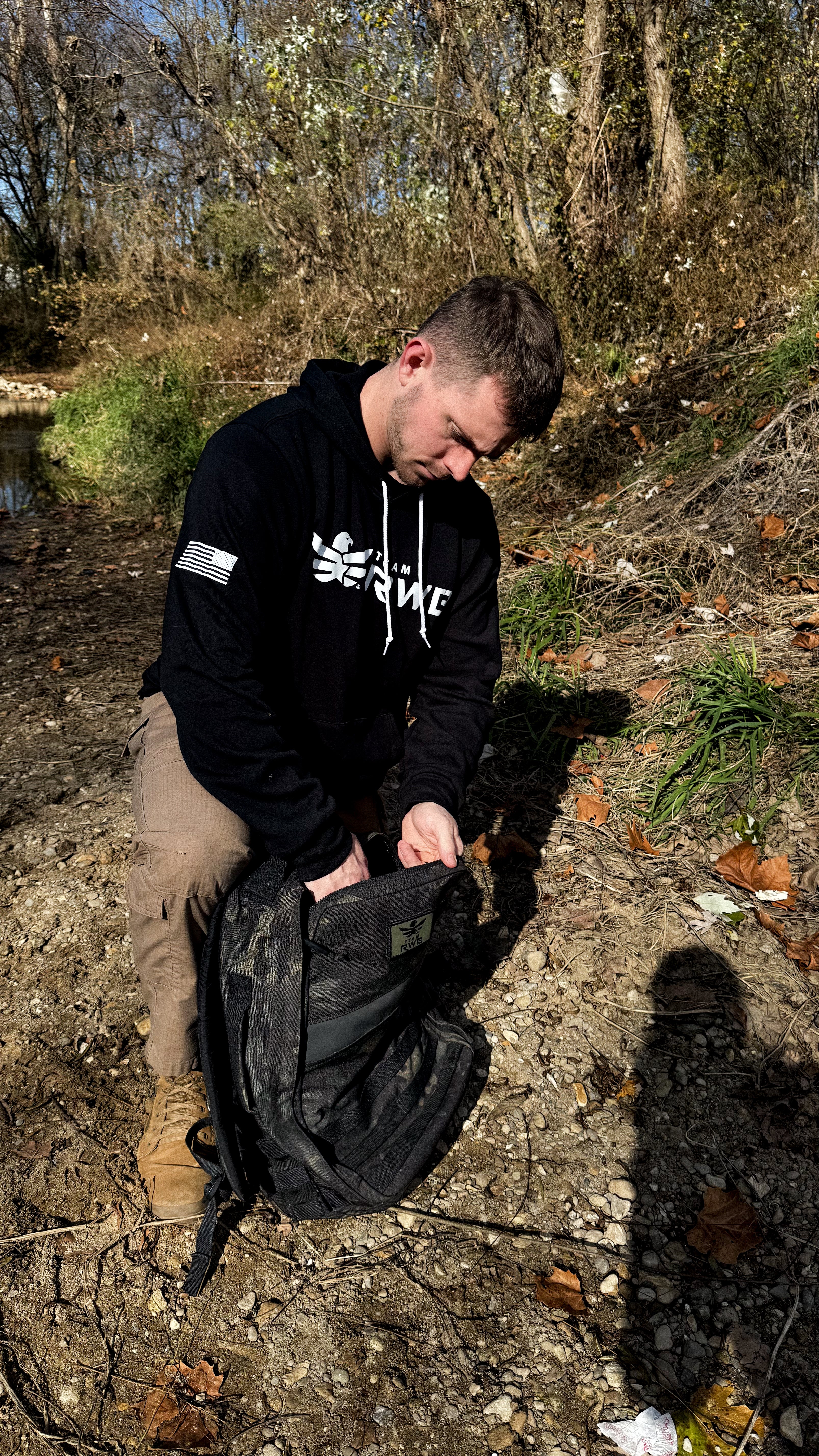 Man wearing black Team RWB hoodie rucking outdoors, side/back view showing fit and sleeve length