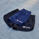 Two pairs of shorts, one blue and one black, with RWB logos on a concrete surface.