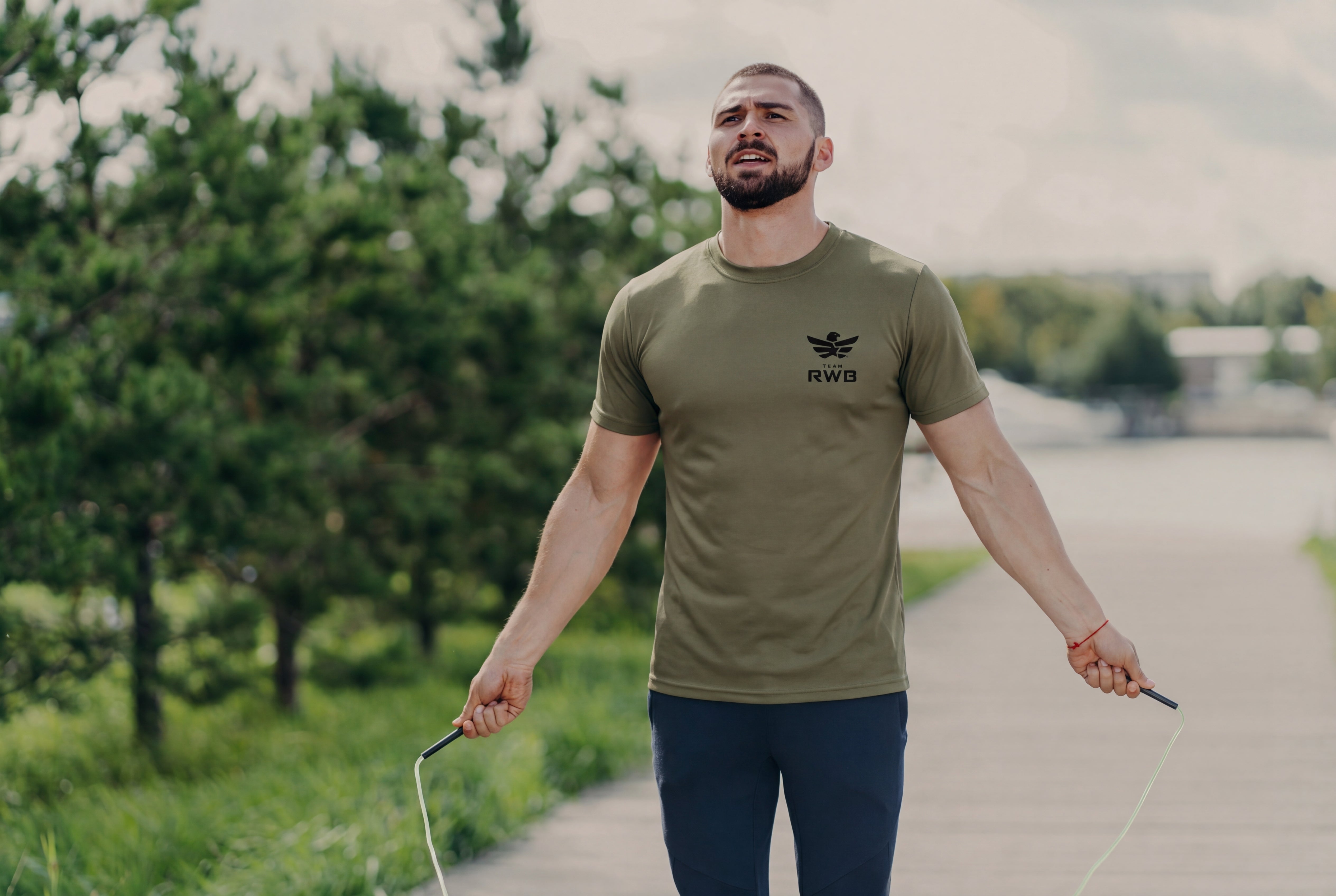 Man holding a jump rope on a path with trees in the background
